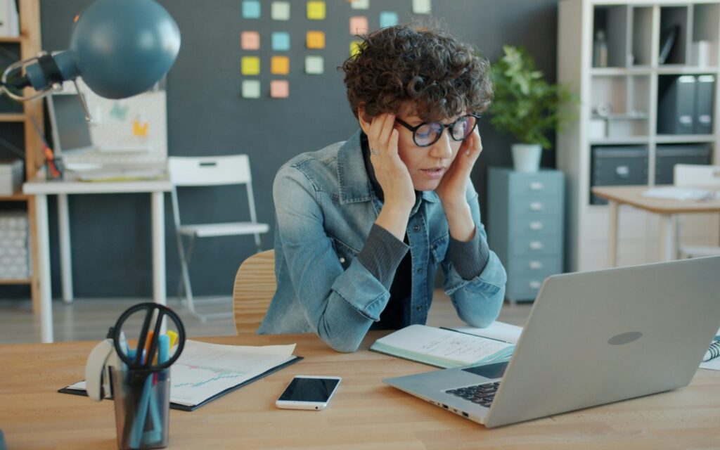 Operational bottlenecks: overwhelmed business owner Business owner with head in hands at a laptop, overwhelmed by an overcomplicated workday